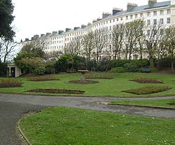 Shows a photograph of Adelaide Crescent. In the foreground is a circular garden display. The background shows a crescent of Regency houses.